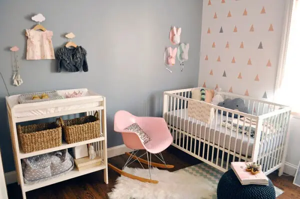 Quarto de bebê cinza e rosa com cabides suspensos e berço branco