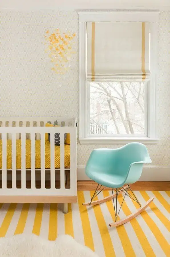 quarto de bebê amarelo decorado com cadeira de balanço azul e tapete listrado Foto Mandarina Studio