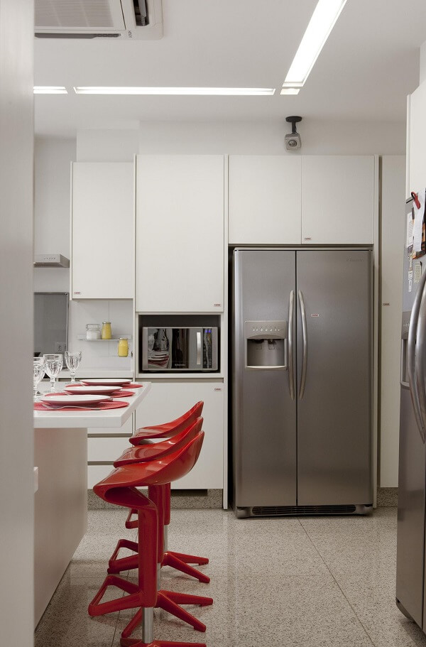 As banquetas vermelhas trazem um toque de cor sobre os pisos para cozinha claros. Fonte: Marcelo Rosset Arquitetura