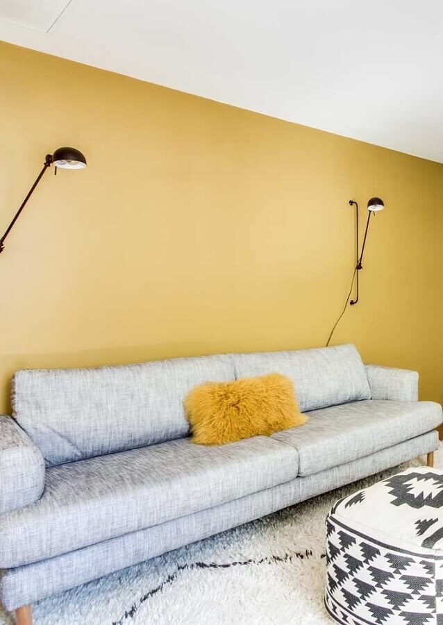 sala com parede amarela decorada com sofá cinza moderno e arandela articulável Foto Dcore Você