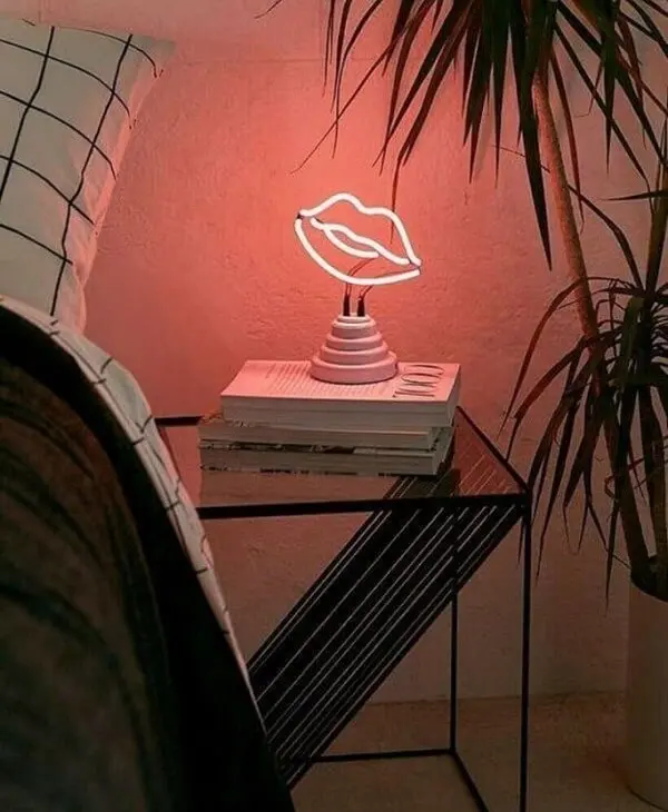 A luminária neon em formato de beijo ilumina a lateral da cama