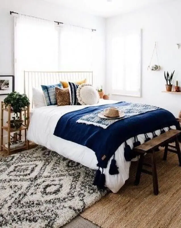quarto de casal todo branco decorado com várias almofadas e peseira azul marinho com detalhes na barra Foto We Heart It