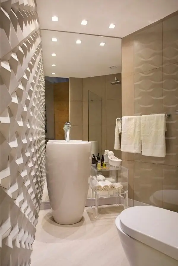 A parede com revestimento para banheiro 3D e a cuba de piso branca se destacam nesse espaço