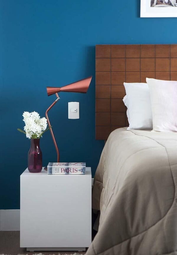 As roupas de cama em tons claros traz neutralidade para o quarto com parede azul