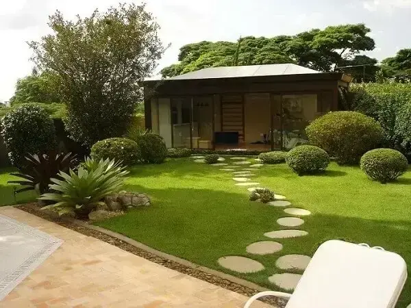 Casa simples com jardim de pedras que formam um caminho até a casa. Projeto de Alalou Paisagismo