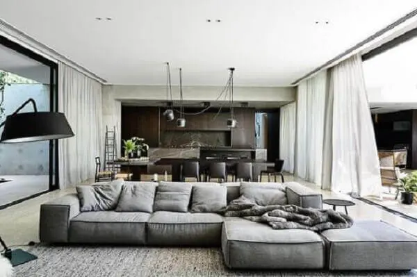 O sofá de canto cinza delimita a área da sala de estar