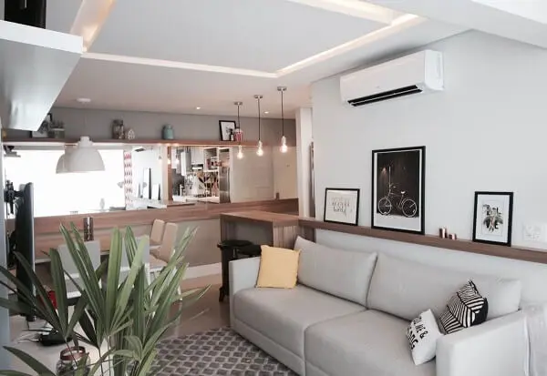 A prateleira alinhada acima do sofá cinza serve de apoio para vários quadros para sala de TV
