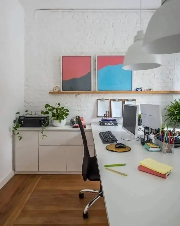 escritório decorado com parede de tijolinho branco e prateleira para quadros de madeira Foto SP Estúdio