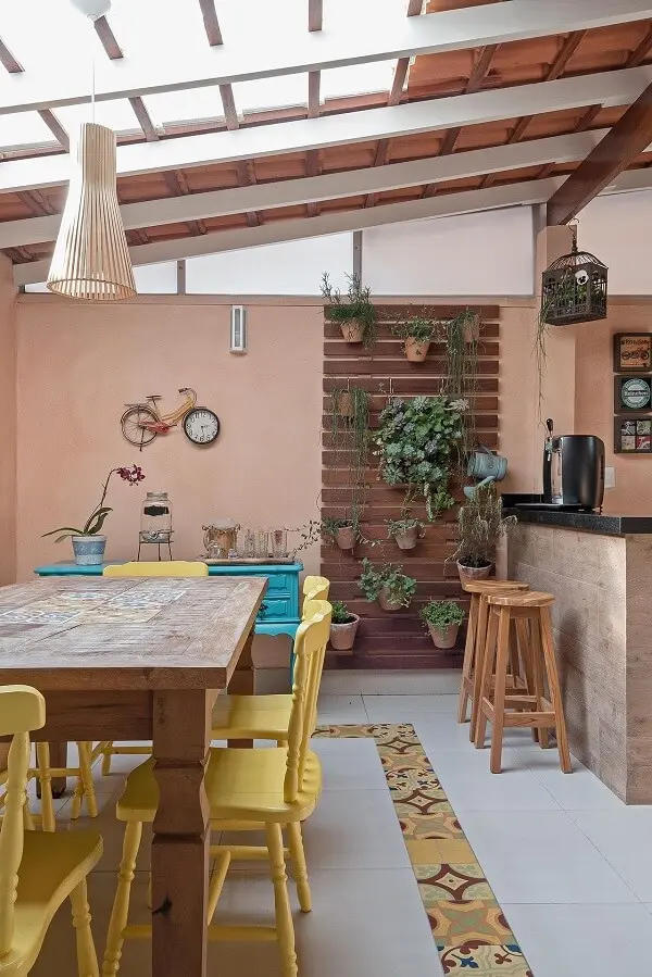 Área gourmet rústica com cadeiras de madeira amarela e piso com ladrilho