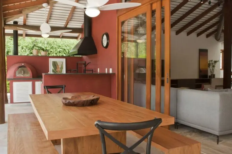 Área gourmet rústica com parede vermelha e mesa de madeira