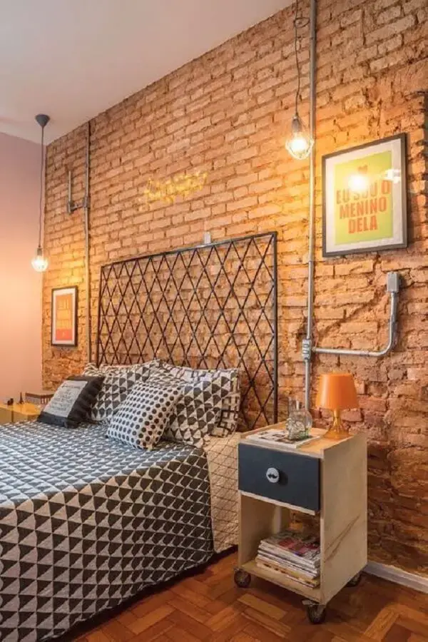 A cama com cabeceira de ferro se conecta com a parede de tijolinho aparente
