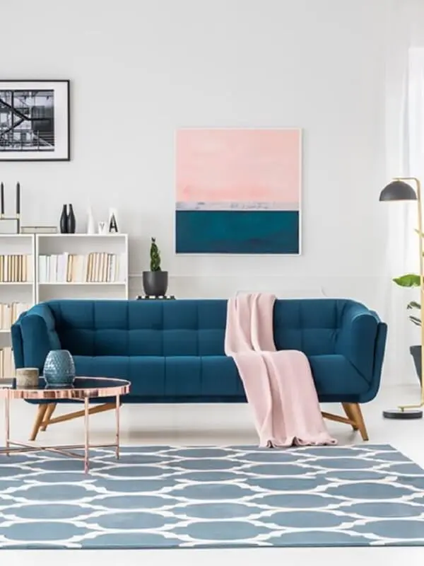 Sofá azul, manta rosa e mesa de centro retrô redonda com acabamento delicado decoram a sala