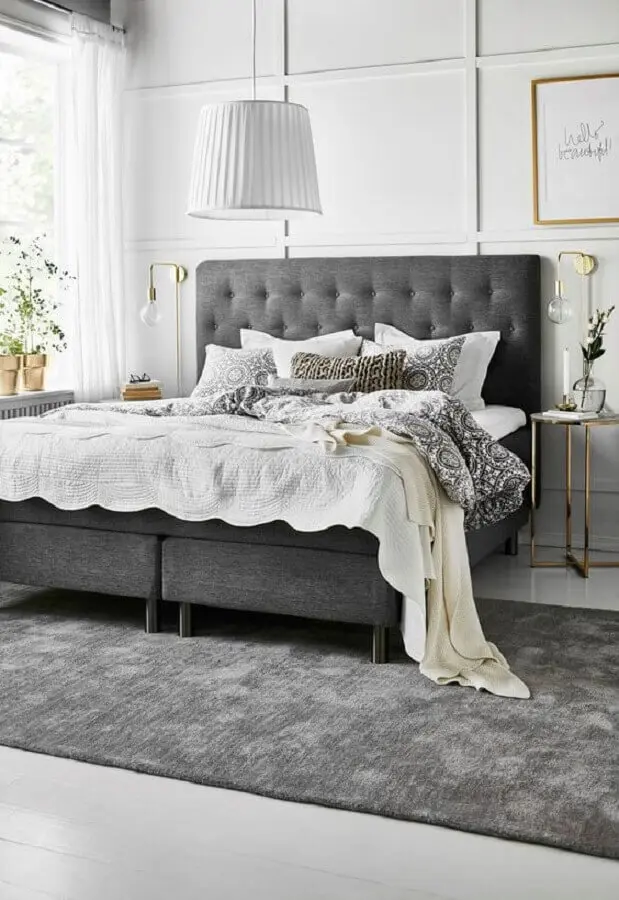 cabeceira estofada cinza para decoração de quarto com mesa de cabeceira redonda e luminária de parede dourada Foto El Mueble