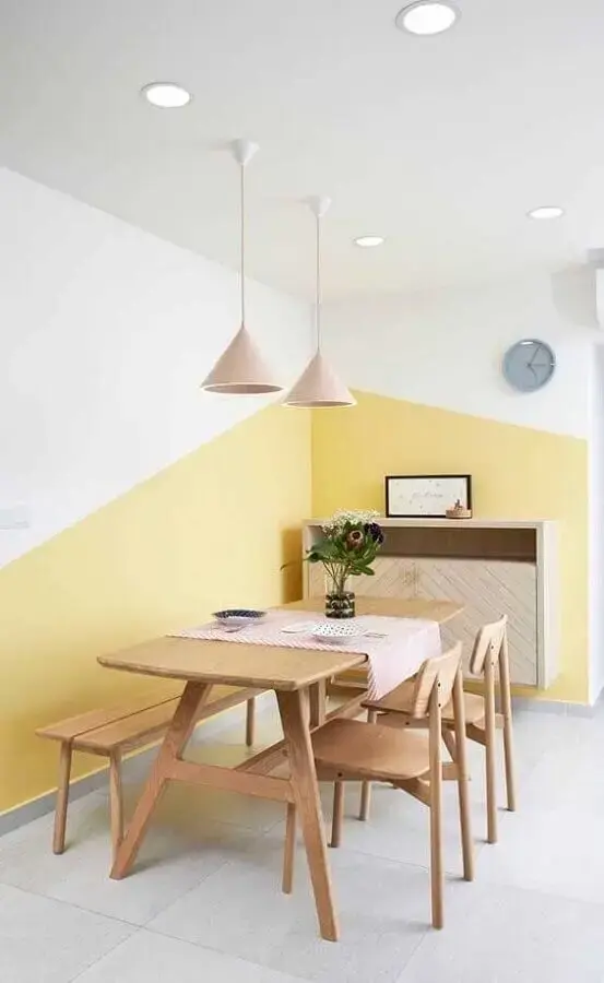 sala de jantar minimalista decorada com mesa de madeira e parede geométrica amarela e branca Foto Jeito de Casa