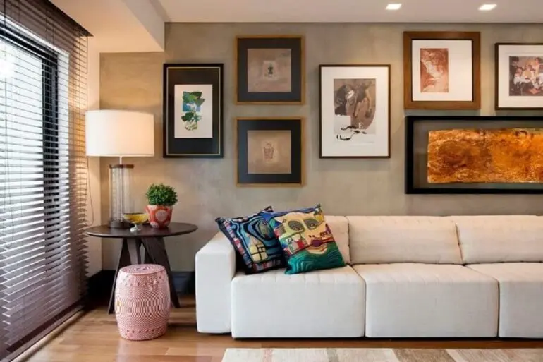 sala moderna e sofisticada decorada com sofá 3 lugares retrátil confortável e parede de cimento queimado com vários quadros Foto Elmor Arquitetura