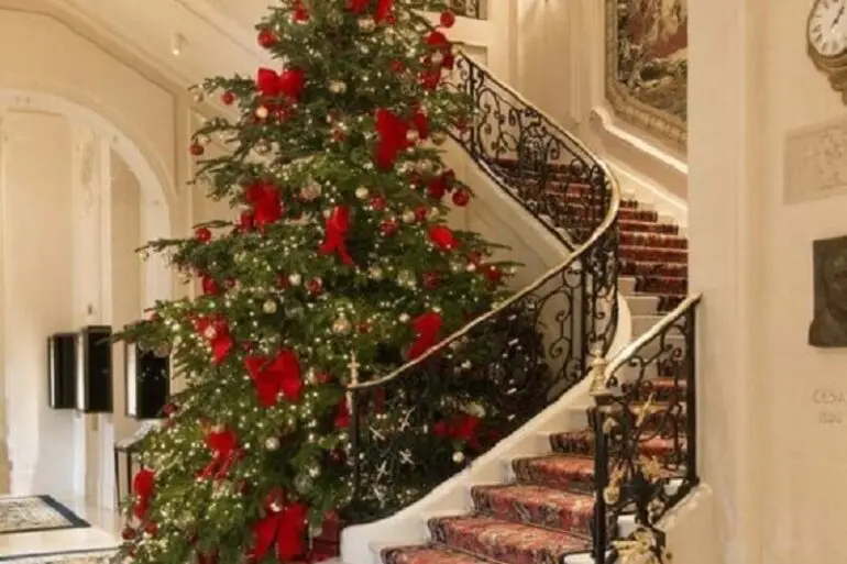 árvore de natal grande com laços vermelhos ao lado de escada Foto The Happy Hideout