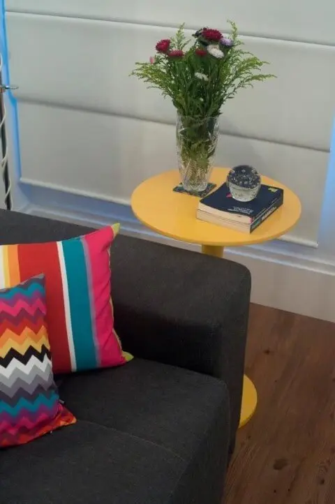 Mesa lateral alta amarela ao lado do sofá cinza