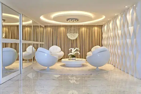 Parede com revestimento 3D e mesa de centro branca redonda complementam a decoração desse espaço