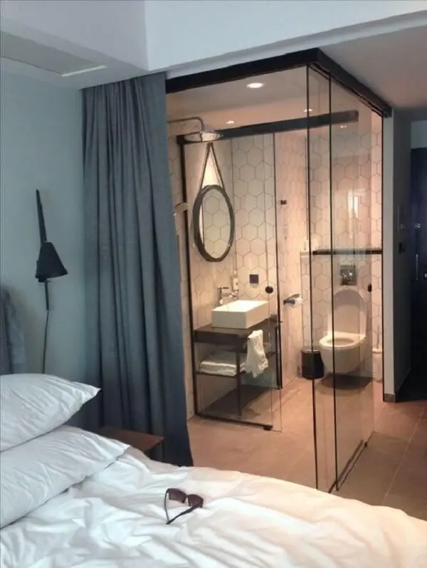 A cortina cinza traz privacidade para o quarto com suíte de vidro
