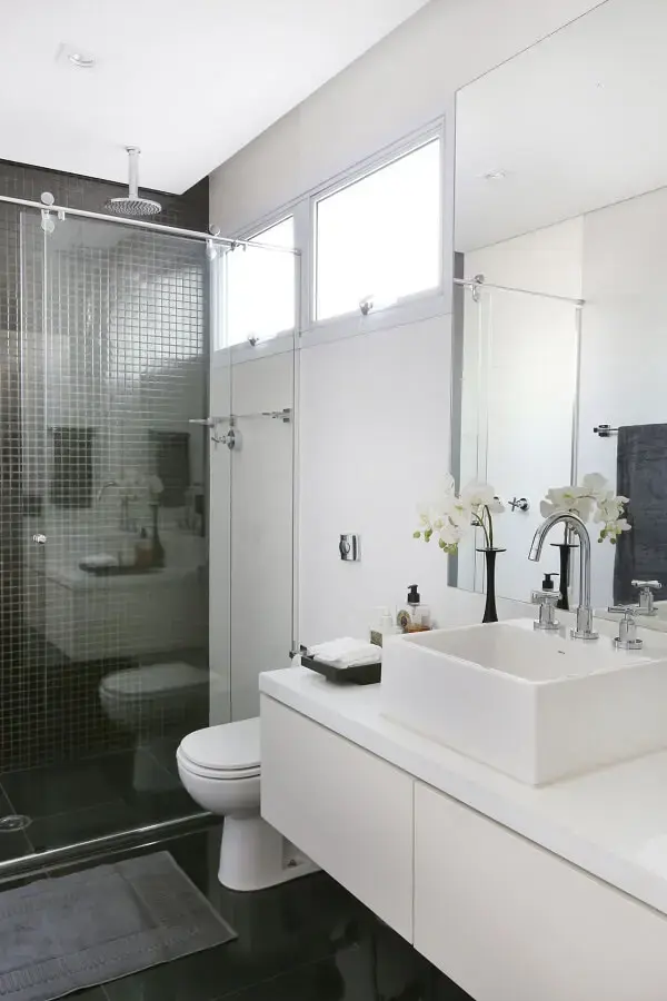 Banheiro branco com pastilhas pretas e chuveiro cromado trazem um ar sofisticado ao espaço