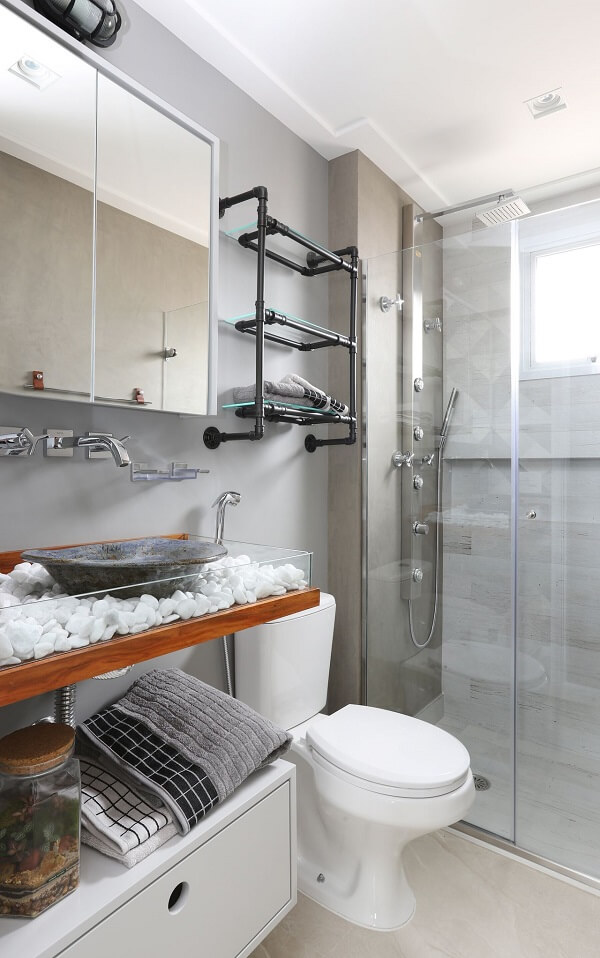 Banheiro com pegada industrial conta com chuveiro cromado quadrado e elementos em tom preto e madeira