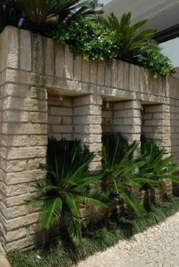 Muro de pedra grés e pequenos coqueiros complementam a jardinagem do local