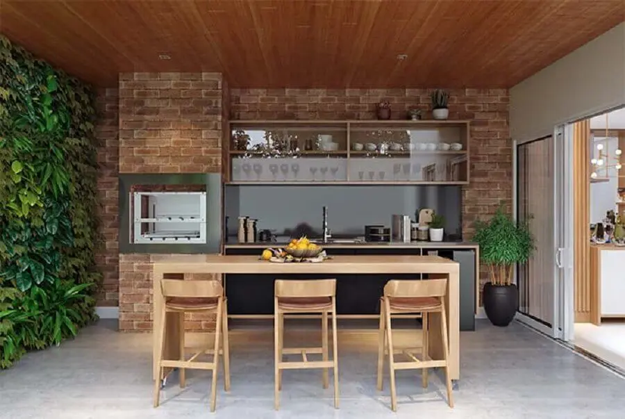 parede de tijolinho para varanda gourmet rústica com churrasqueira e bancada de madeira Foto Jeito de Casa