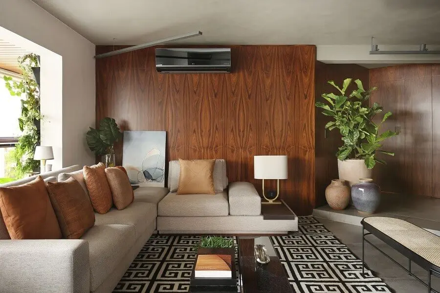 sala com sofá bege de canto decorada com tapete geométrico e parede de madeira Foto Quattrino Arquitetura