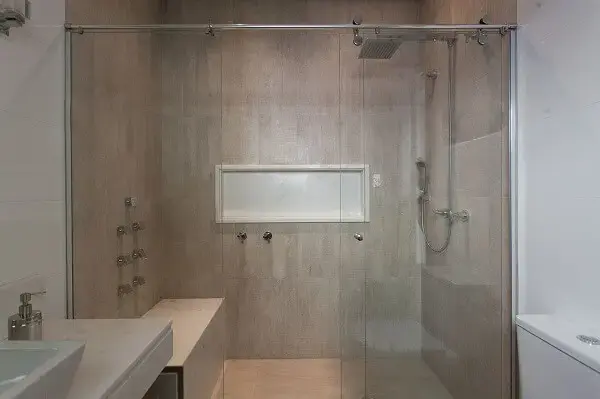 Área de banho ampla revestida com porcelanato e chuveiro cromado quadrado