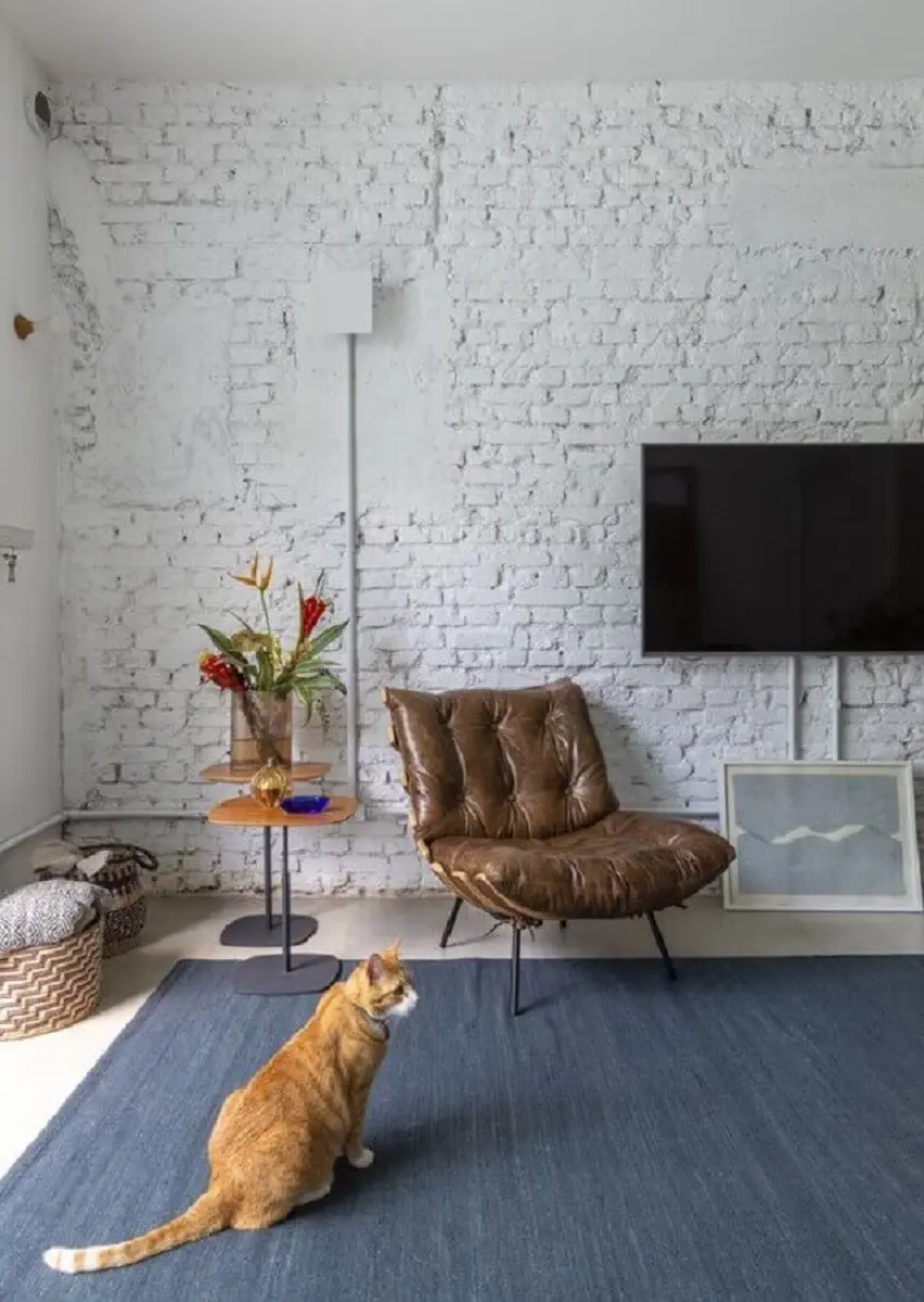 sala de TV decorada com parede tijolinho branca e poltrona de couro marrom escuro Foto INÁ Arquitetura