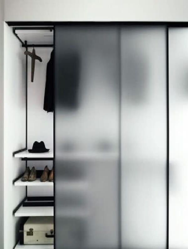 O guarda-roupa com porta de correr para quarto de vidro esconde parcialmente roupas e sapatos