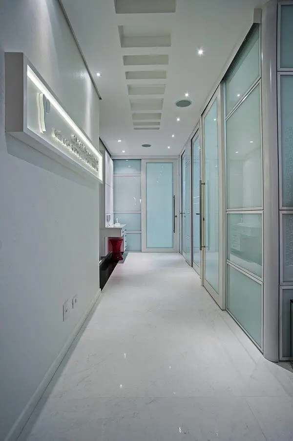 Corredor com portas de vidro e pontos e luminária para corredor embutida no teto discreta