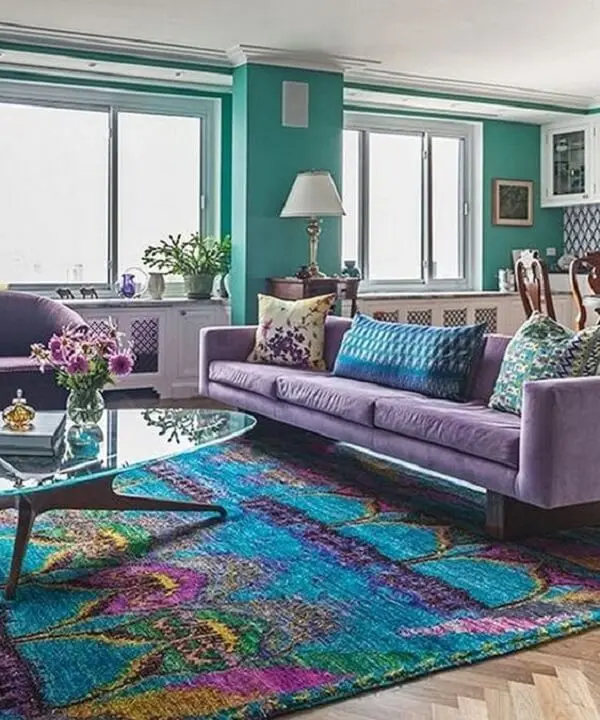 O sofá roxo de 3 lugares conversa diretamente com o tapete estampado