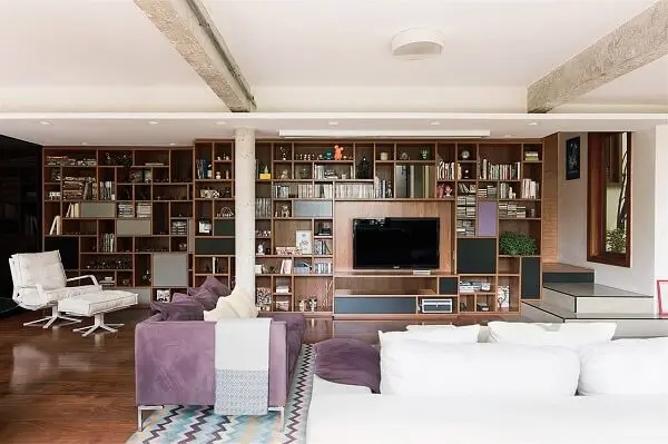 O tapete com estampa geométrica apresenta nuances em roxo conversando diretamente com o sofá roxo do local