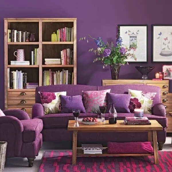 Os móveis em madeira trazem um contraste para a poltrona e sofá roxo