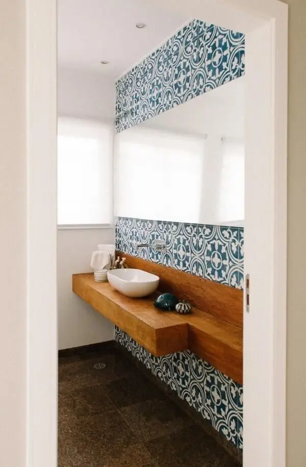 Parede com ladrilho azul e bancada de madeira com cuba de apoio para banheiro formam uma combinação harmoniosa