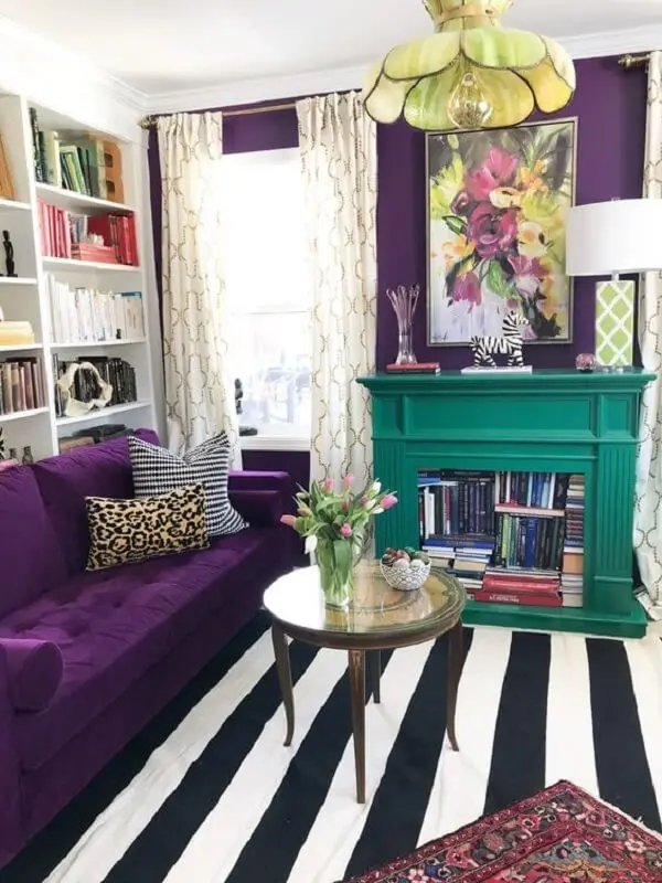 Sofá roxo escuro com tapete listrado decoram o espaço