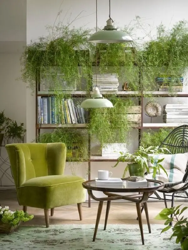 A poltrona pé palito verde se mistura em meio as plantas da sala de estar