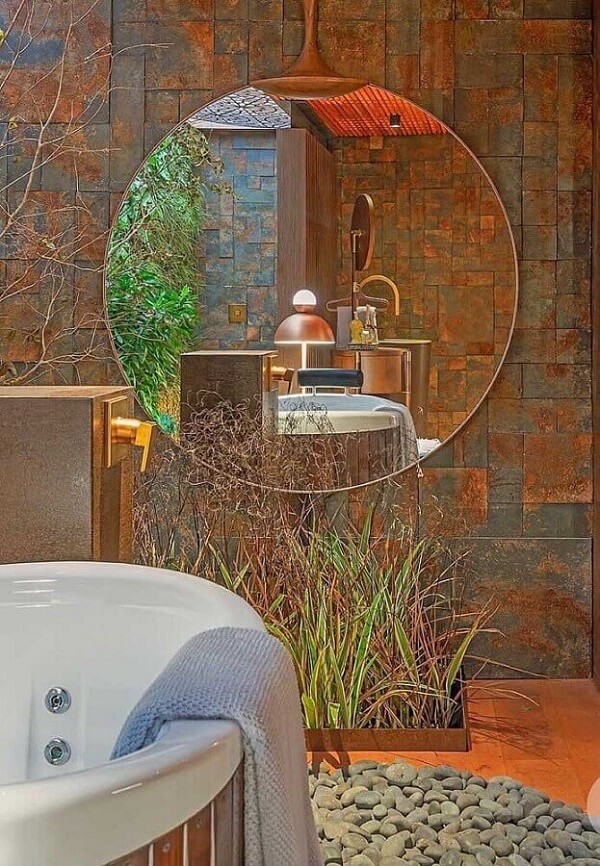 Decoração de banheiro com banheira, espelho redondo e revestimento de pedra ferro