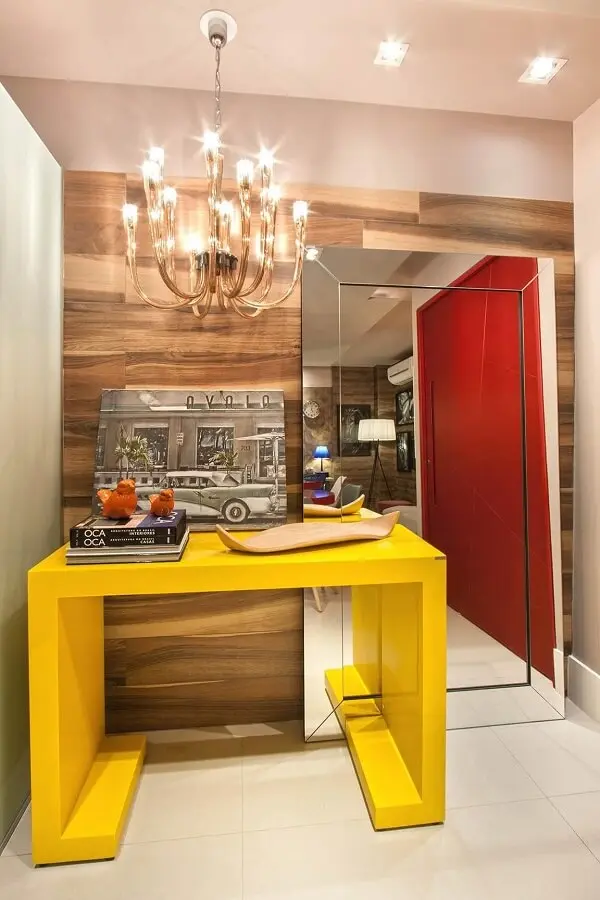 O aparador amarelo com espelho de chão decoram o hall de entrada do imóvel