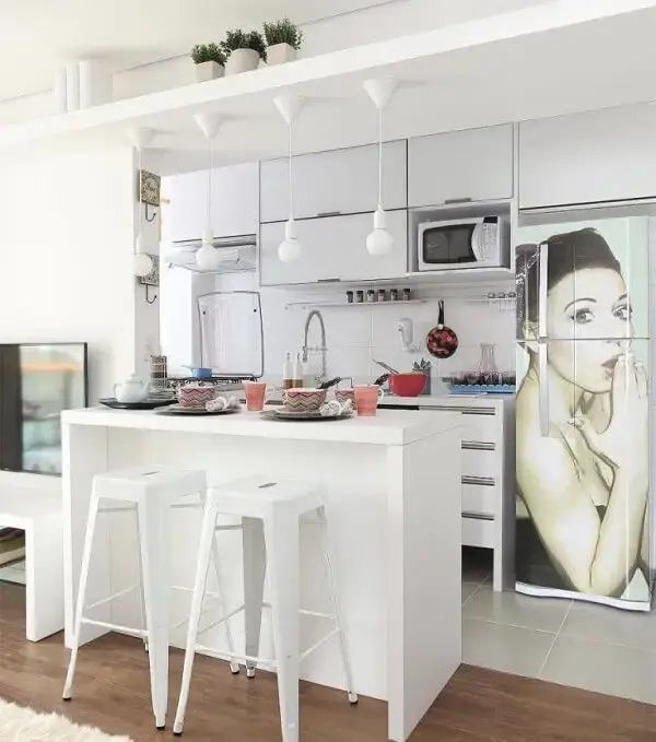 O armário basculante cozinha branco traz neutralidade para o espaço com geladeira adesivada.