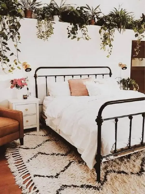 Quarto romântico decorado com vários vasos de plantas, cama de ferro e mesa de cabeceira retrô branca com gavetas