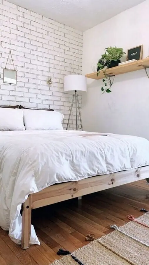 Decoração de quarto de casal simples com parede de tijolinho branco e cama de madeira
