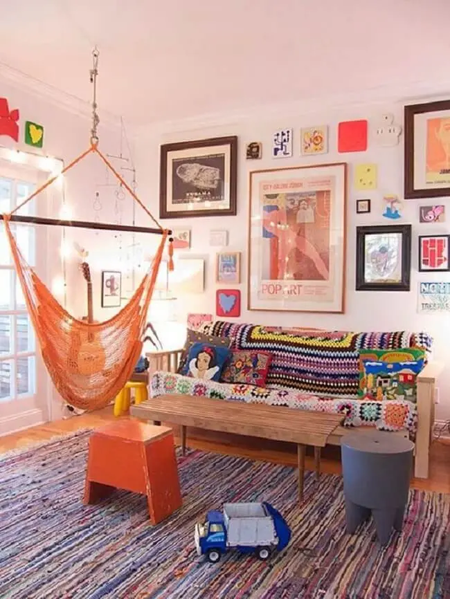 A cadeira de rede laranja se mistura na decoração da sala de estar