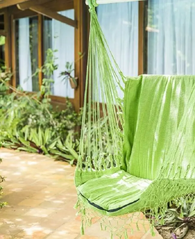 O tom verde da cadeira de balanço rede se mistura com as plantas do jardim