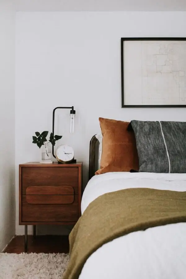 quarto branco decorado com várias almofadas e criado mudo de madeira Foto Jeito de Casa