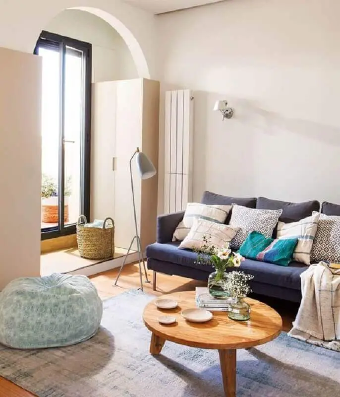 sala simples decorada com mesa de centro redonda de madeira e sofá azul marinho Foto El Mueble