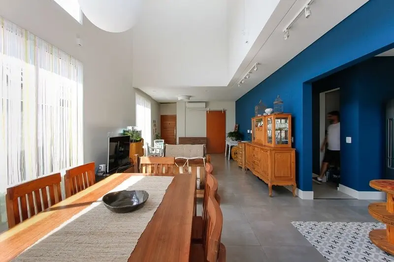 Móveis em madeira, piso fosco e paredes azuis marcam a decoração do espaço. Projeto por Otoni Arquitetura