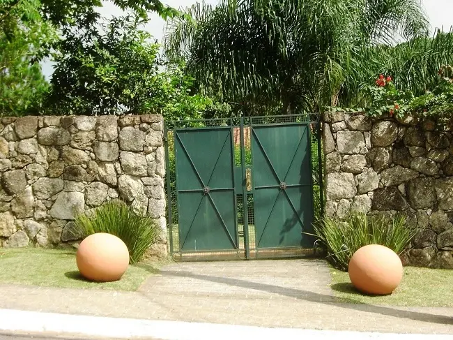 Fachada com portão verde e revestimento externo com pedras. Projeto de Luciana Wehba