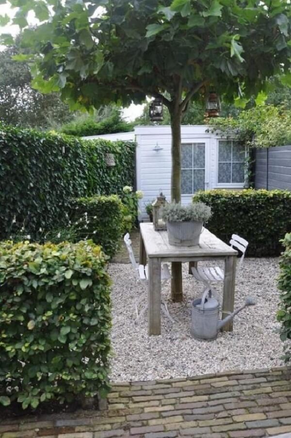 Jardim com pedra branca e mesa de madeira formam um ambiente aconchegante. Fonte: Pinterest